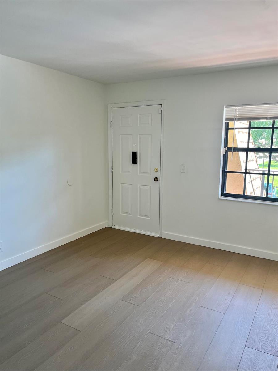 An empty room features light wood-look flooring, white walls, a white door, and a window — 4243 Oak Terrace Drive # 4243, FL 33463, FL