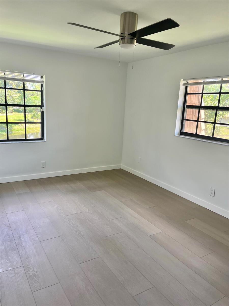 An empty bedroom features light wood-look flooring, white walls, a ceiling fan, and two windows — 4243 Oak Terrace Drive # 4243, FL 33463, FL