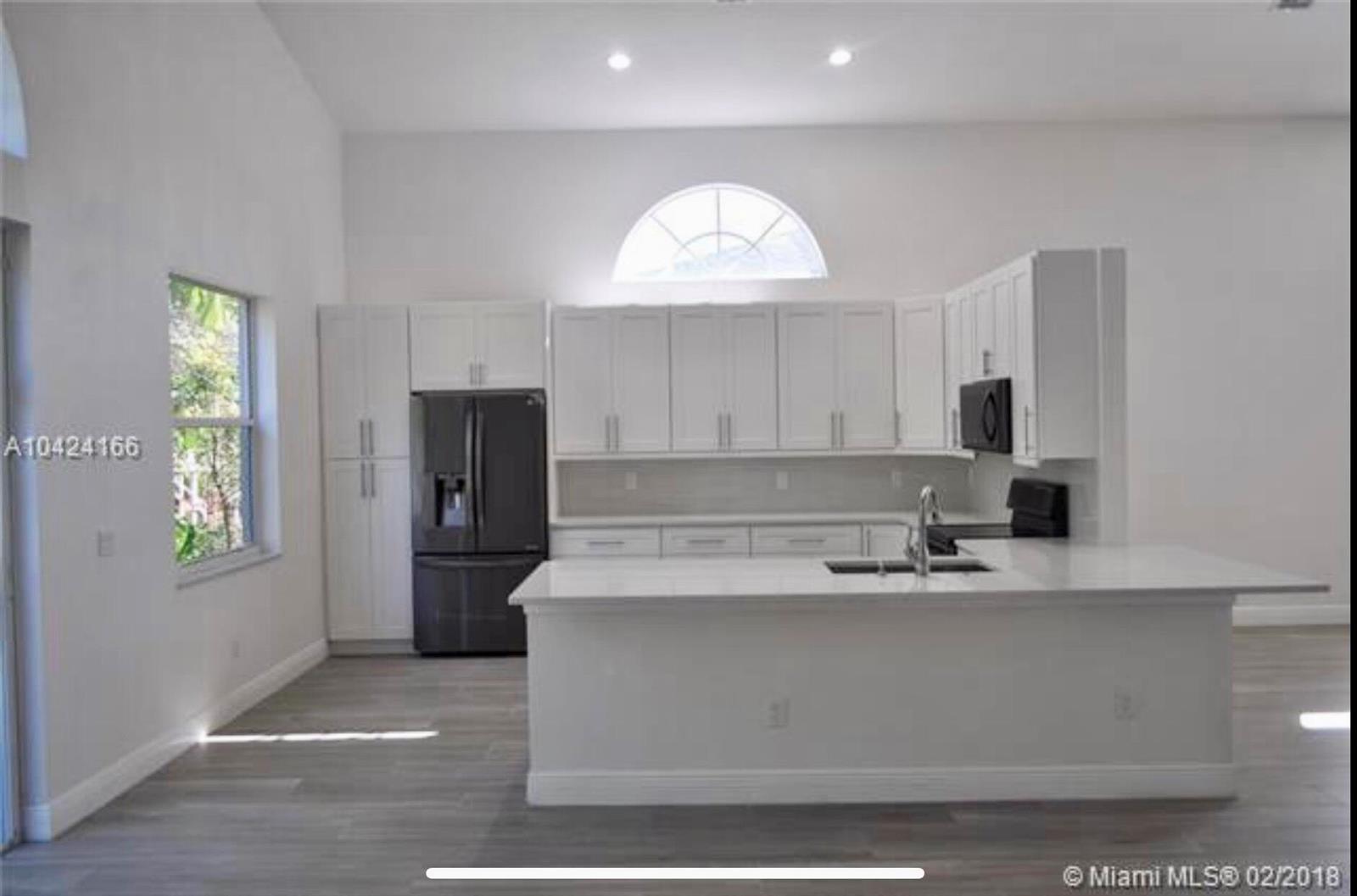 A modern kitchen features white cabinetry, a large island, and a black refrigerator — 5 Lake Eden Drive, Boynton Beach FL 33435, BOYNTON BEACH, FL