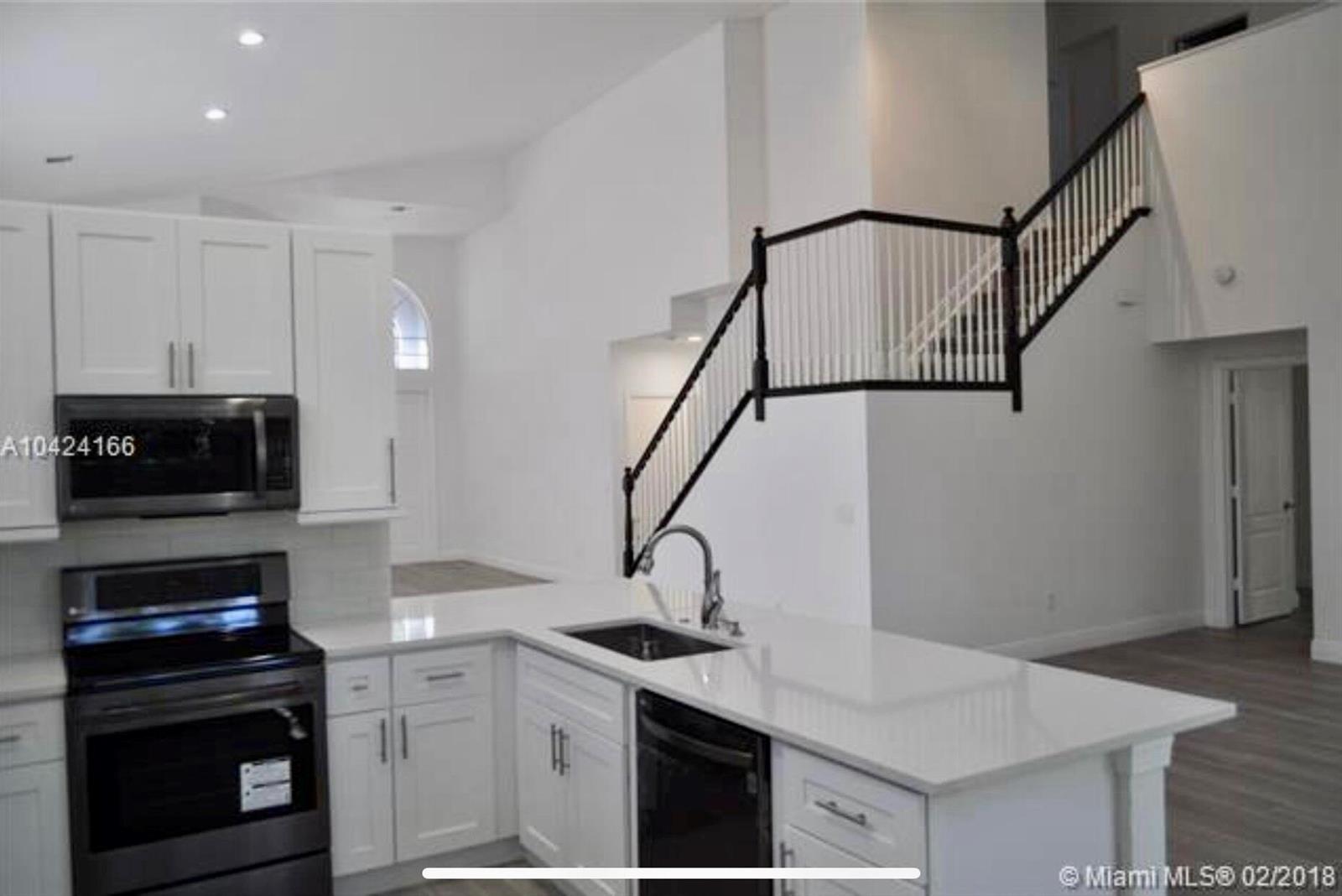 A kitchen with white cabinets and a quartz island overlooks a staircase with black railings — 5 Lake Eden Drive, Boynton Beach FL 33435, BOYNTON BEACH, FL