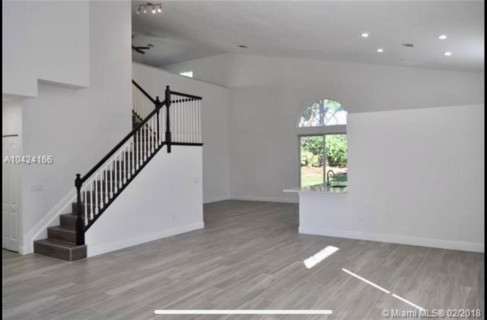 An open-concept living area features light wood-look flooring, a staircase with black railings, and recessed lighting — 5 Lake Eden Drive, Boynton Beach FL 33435, BOYNTON BEACH, FL
