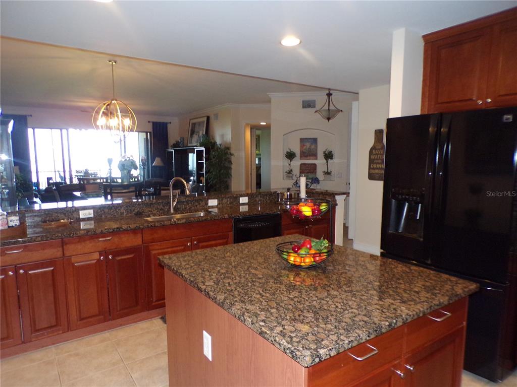 A kitchen features dark wood cabinets, granite countertops, a central island, and a black refrigerator — 89 VIVANTE BOULEVARD UNIT 205, PUNTA GORDA, FL