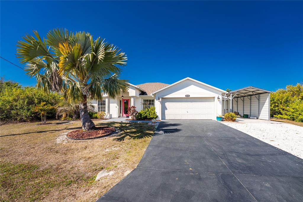 A single-story house features a white exterior, a two-car garage, and a large palm tree — 9300 MIAMI CIRCLE, PORT CHARLOTTE, FL