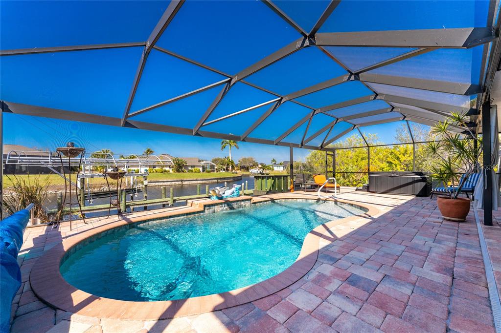 A screened-in pool patio features a kidney-shaped pool, brick pavers, and a canal view — 9300 MIAMI CIRCLE, PORT CHARLOTTE, FL