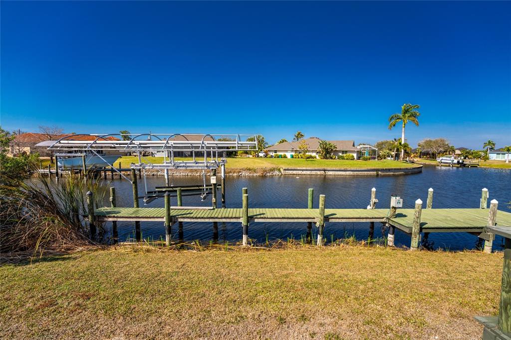 A wooden dock with a boat lift extends into a canal behind a grassy yard — 9300 MIAMI CIRCLE, PORT CHARLOTTE, FL