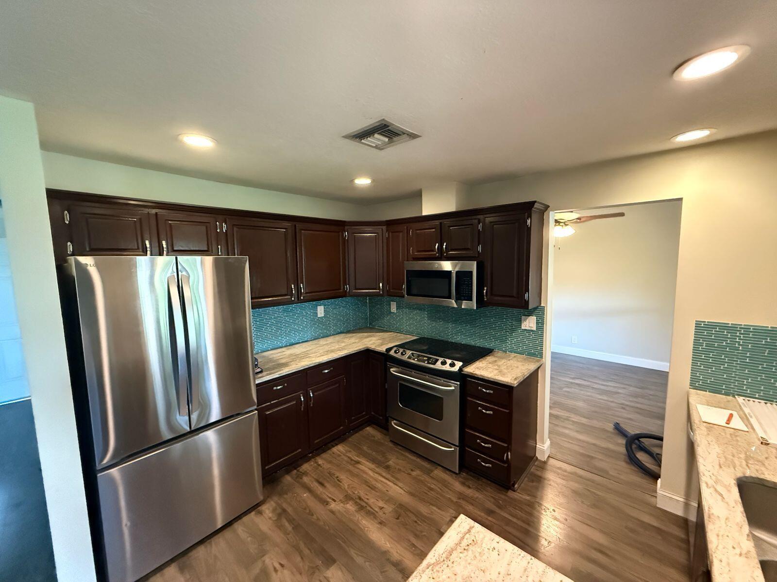 A kitchen features dark wood cabinets, stainless steel appliances, and a blue glass tile backsplash — 13584 Exotic lane, Wellington FL 33514, WELLINGTON, FL