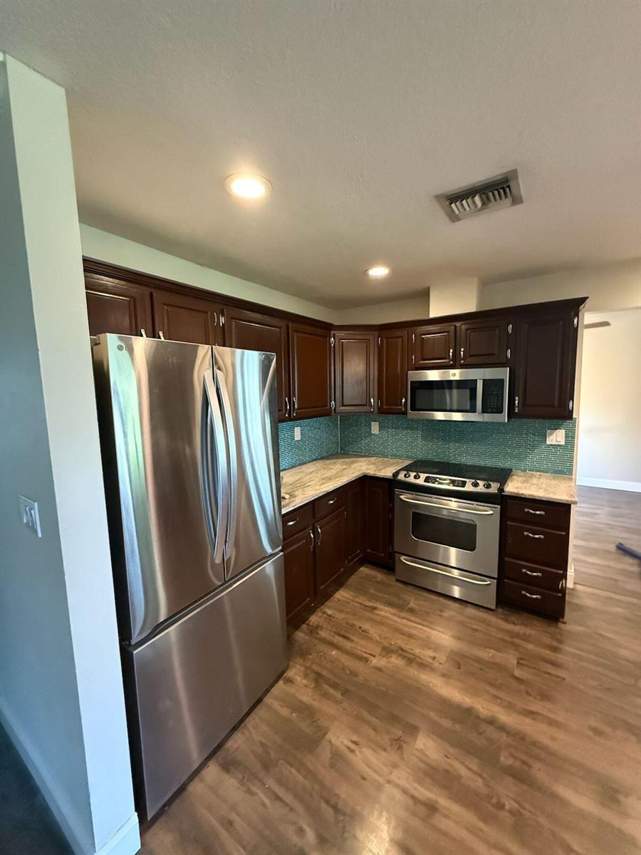 A kitchen features dark wood cabinets, stainless steel appliances, light countertops, and a teal backsplash — 13584 Exotic lane, Wellington FL 33514, WELLINGTON, FL