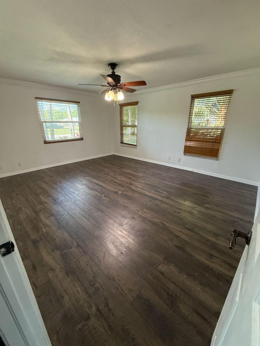 An empty room with dark wood-look flooring, white walls, a ceiling fan, and three windows — 13584 Exotic lane, Wellington FL 33514, WELLINGTON, FL