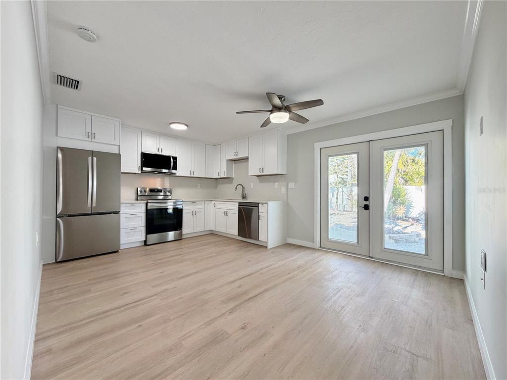 A kitchen with white cabinets, stainless steel appliances, and light wood flooring leads to doors — 13299 3RD STREET E UNIT S, MADEIRA BEACH, FL