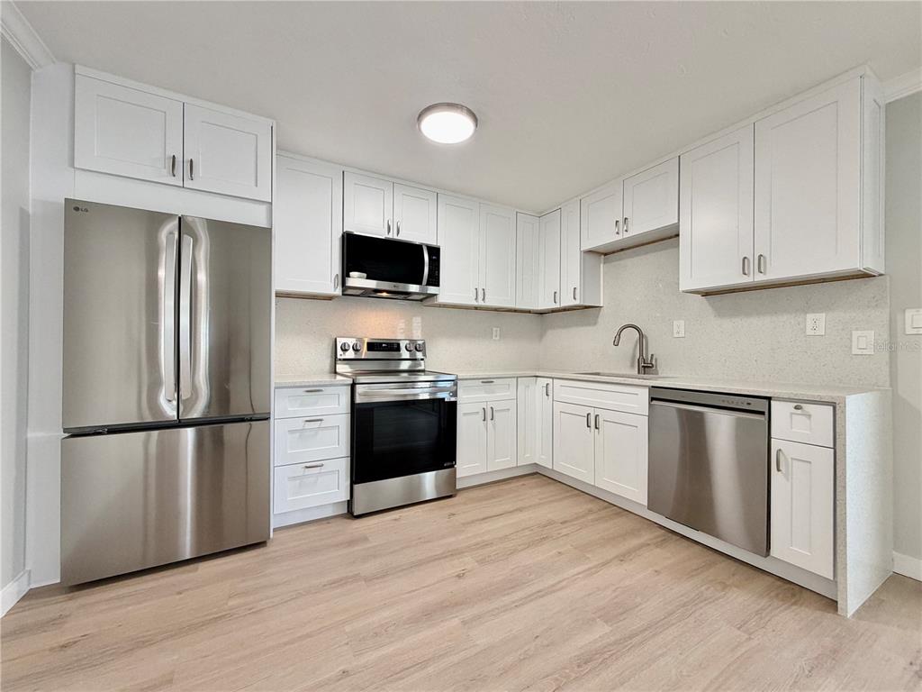 A kitchen features white shaker cabinets, stainless steel appliances, and light wood-look flooring — 13299 3RD STREET E UNIT S, MADEIRA BEACH, FL