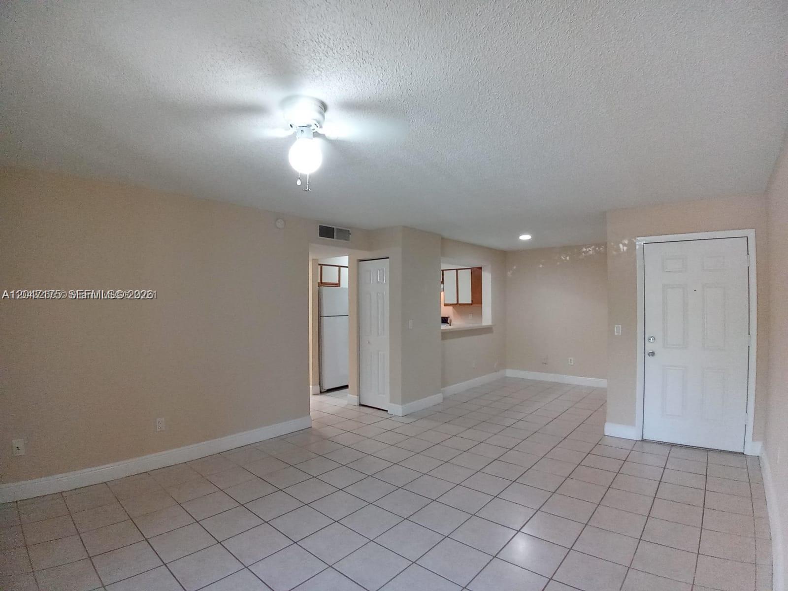 An interior view of a room with beige walls, tiled floors, a ceiling fan, and a kitchen — POMPANO BEACH, FL