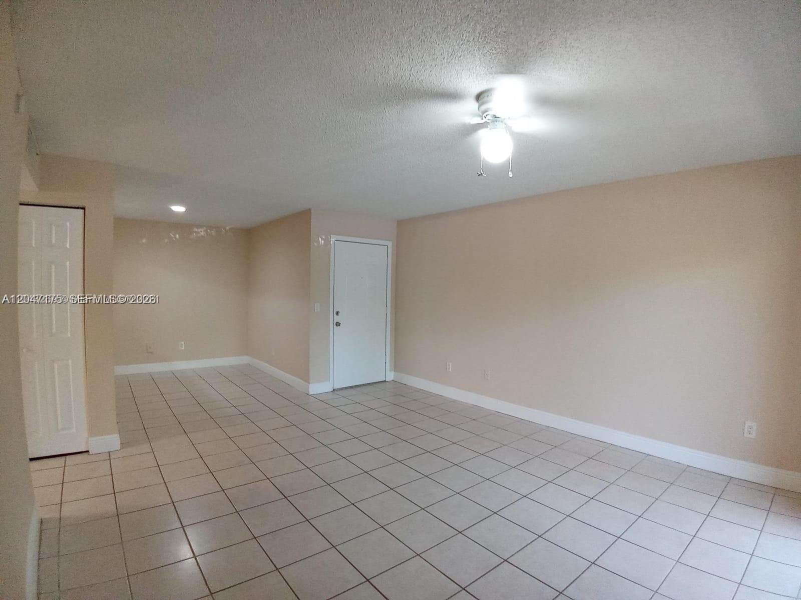 An empty room features beige walls, white baseboards, a tiled floor, and a ceiling fan — POMPANO BEACH, FL