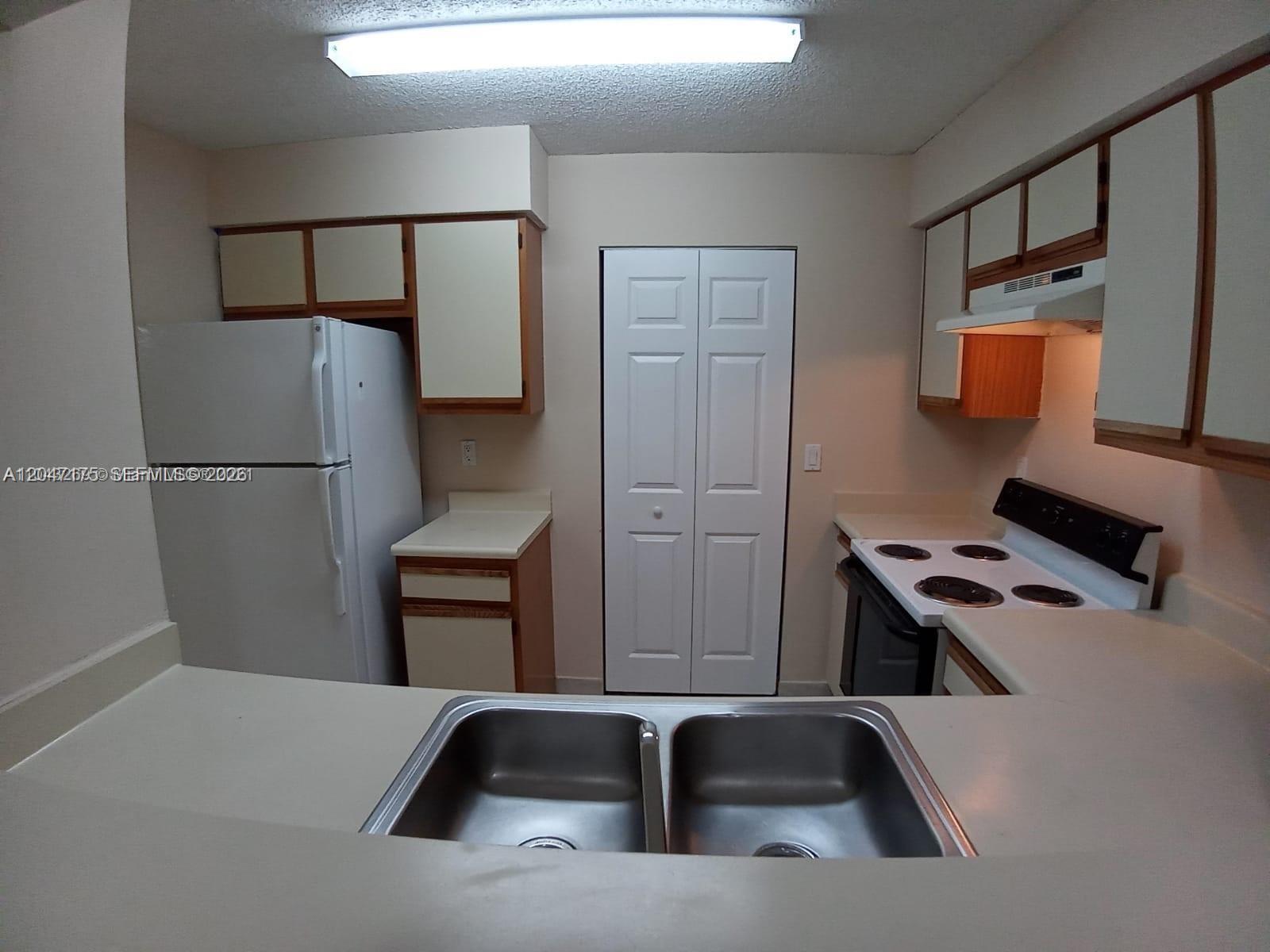 A kitchen features white appliances, wood-trimmed cabinets, a double sink, and a central pantry door — POMPANO BEACH, FL