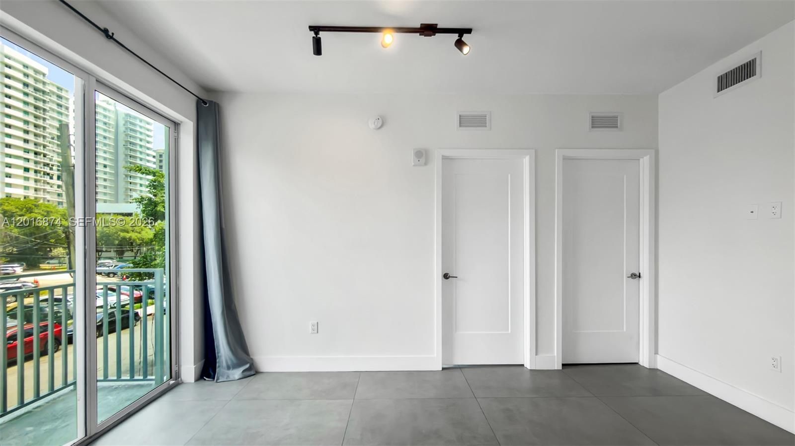 A minimalist room features gray tile flooring, white walls, two doors, and a sliding glass door — 1536 NW 15th Ave # 206, Miami FL 33125, MIAMI, FL
