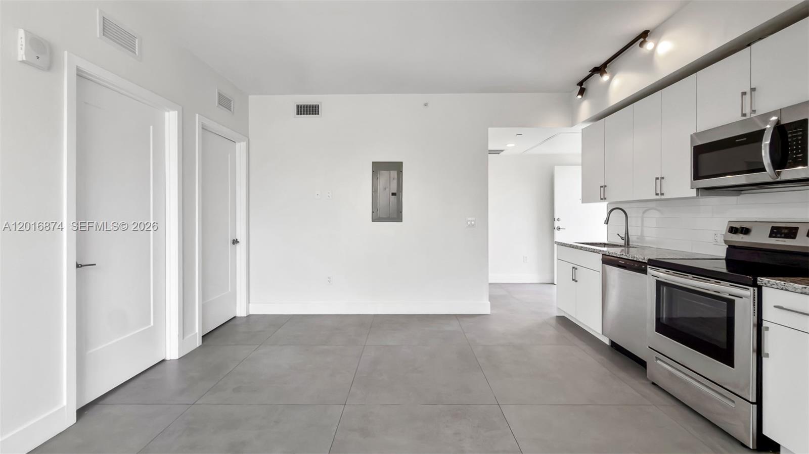 A modern kitchen features white cabinets, stainless steel appliances, and gray tile flooring — 1536 NW 15th Ave # 206, Miami FL 33125, MIAMI, FL
