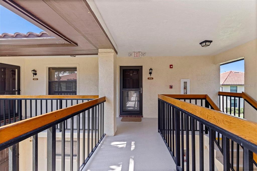 An outdoor walkway leads to a building entrance with a dark door and railings — 809 HAMMOCK PINE BOULEVARD, CLEARWATER, FL