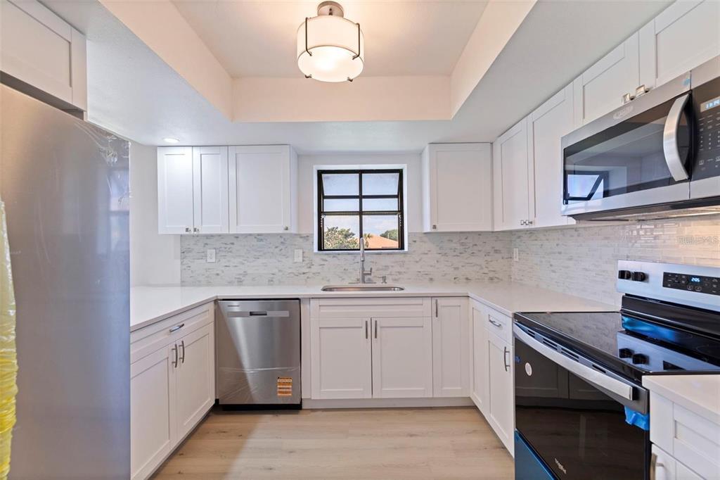 A kitchen with white cabinets, stainless steel appliances, a tiled backsplash, and light wood flooring — 809 HAMMOCK PINE BOULEVARD, CLEARWATER, FL