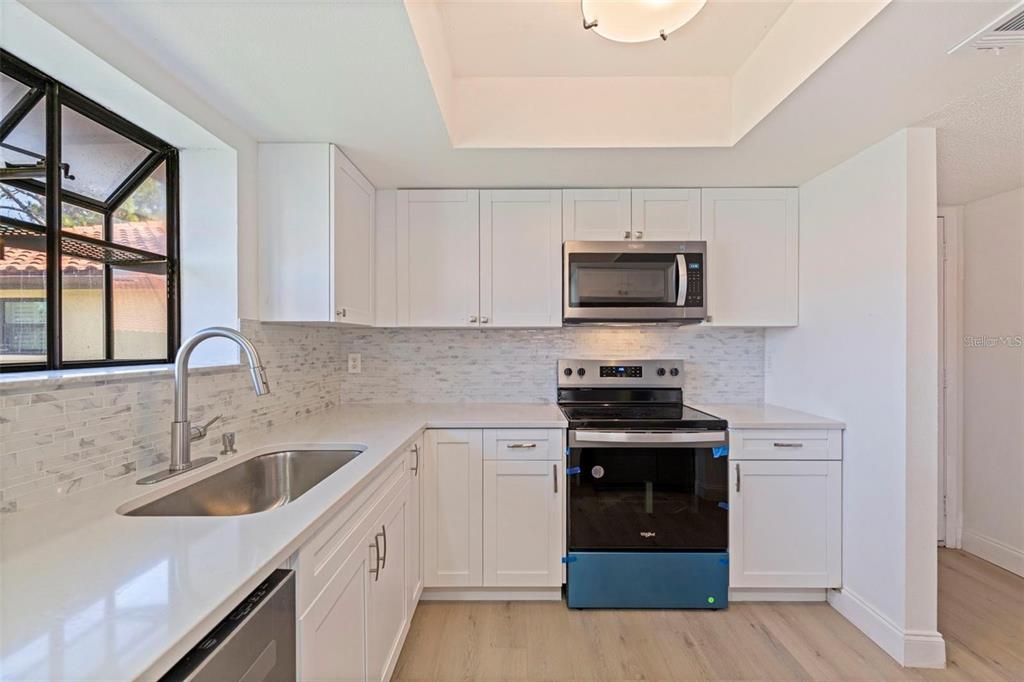A kitchen with white cabinets, stainless steel appliances, a tile backsplash, and a window — 809 HAMMOCK PINE BOULEVARD, CLEARWATER, FL