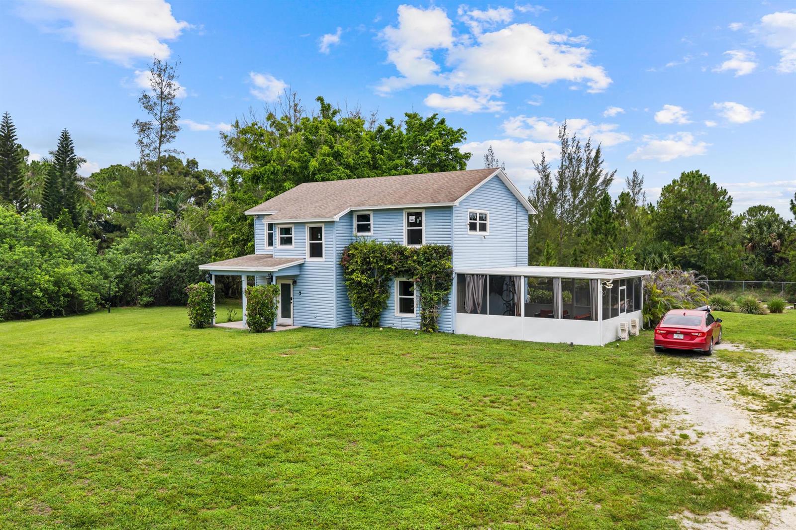 A two-story light blue house with a screened-in porch and a red car parked nearby — 16931 93rd Road N, Loxahatchee FL 33470, LOXAHATCHEE, FL