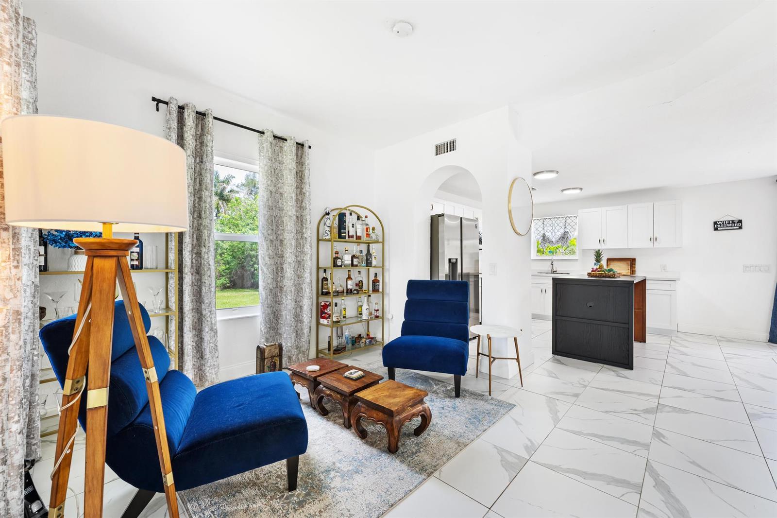A living area with two blue chairs, wooden tables, and a bar cart near a kitchen — 16931 93rd Road N, Loxahatchee FL 33470, LOXAHATCHEE, FL