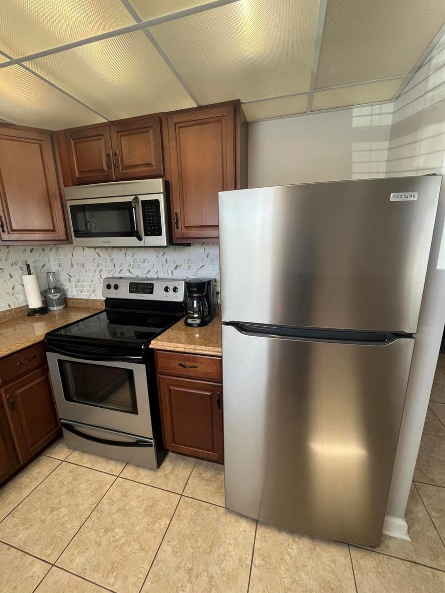 A kitchen features stainless steel appliances, wood cabinets, tan countertops, and light-colored tile flooring — 289 Brittany G, Delray Beach FL 33446, DELRAY BEACH, FL