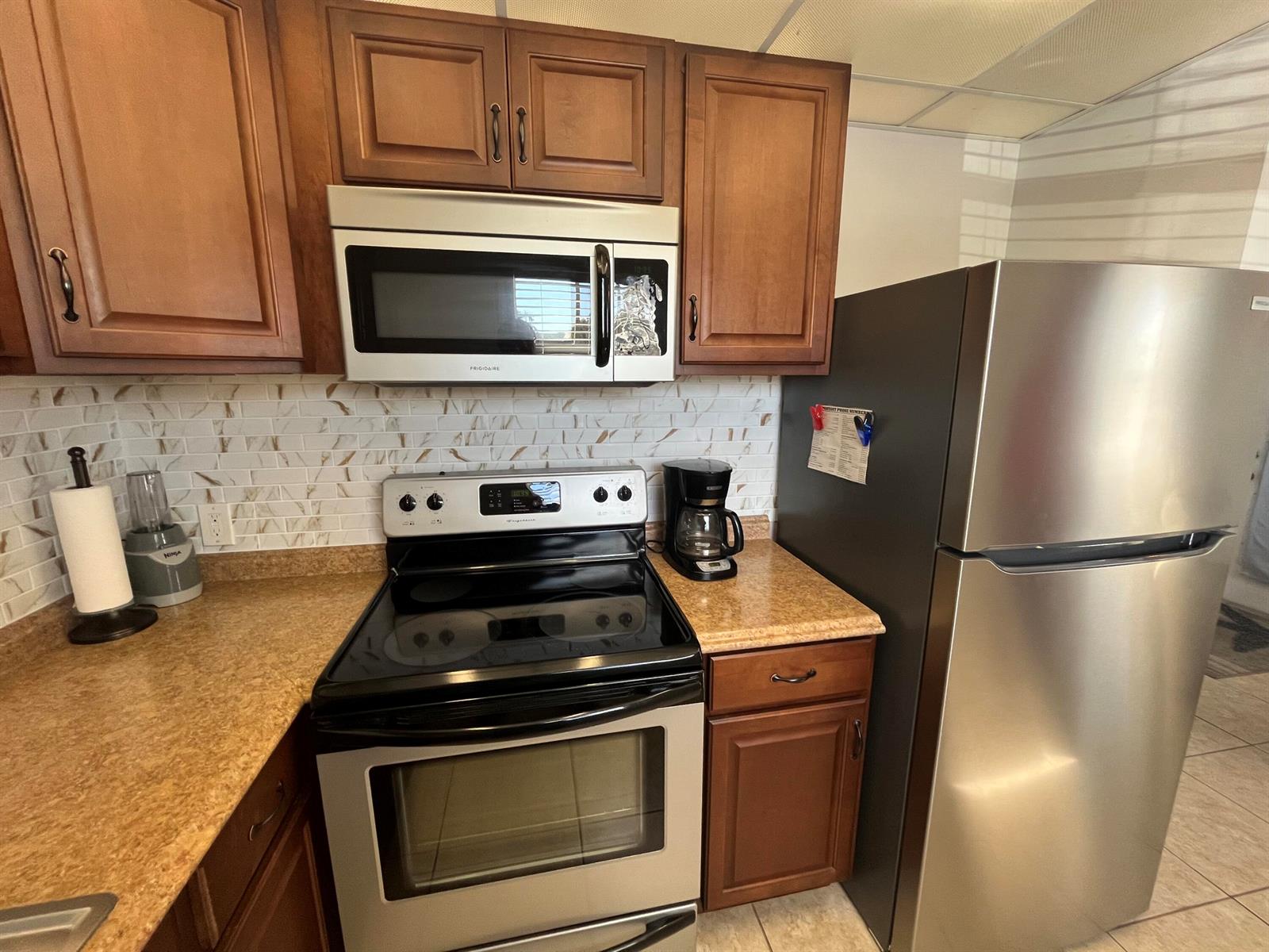 A kitchen features wood cabinets, stainless steel appliances, a tiled backsplash, and tan countertops — 289 Brittany G, Delray Beach FL 33446, DELRAY BEACH, FL