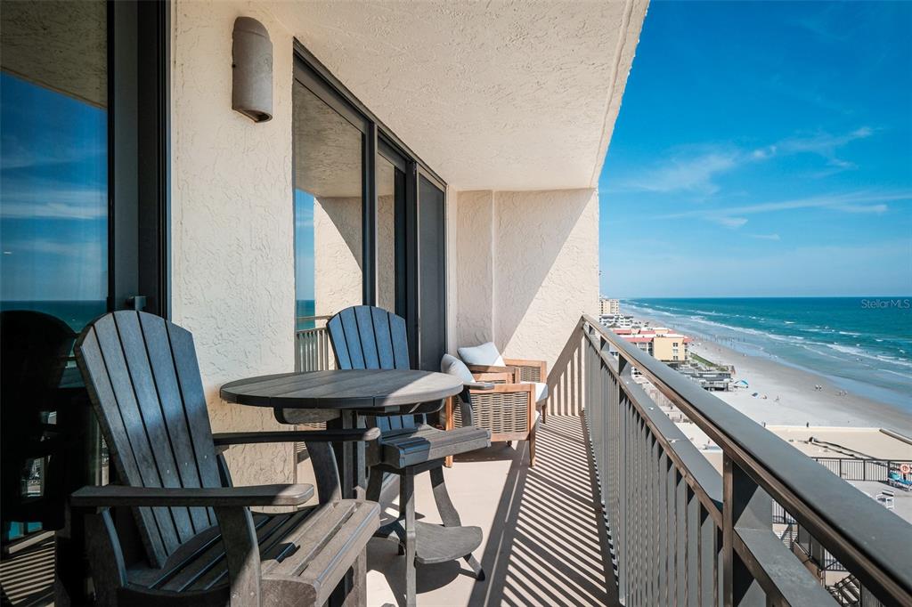A balcony with outdoor furniture overlooks a sandy beach and the ocean under a blue sky — 4139 S ATLANTIC AVENUE UNIT B508, NEW SMYRNA BEACH, FL