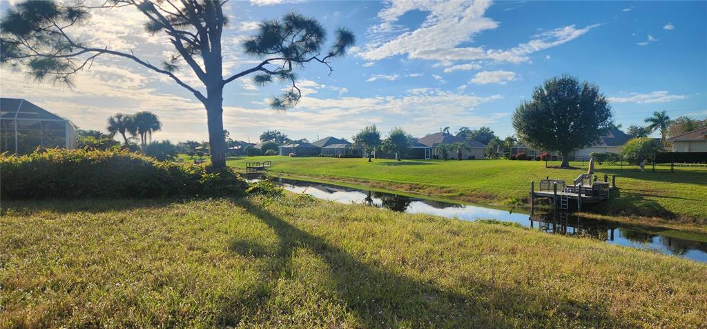 A grassy backyard overlooks a narrow canal with a wooden dock and residential homes nearby — 437 ROTONDA CIRCLE, ROTONDA WEST, FL
