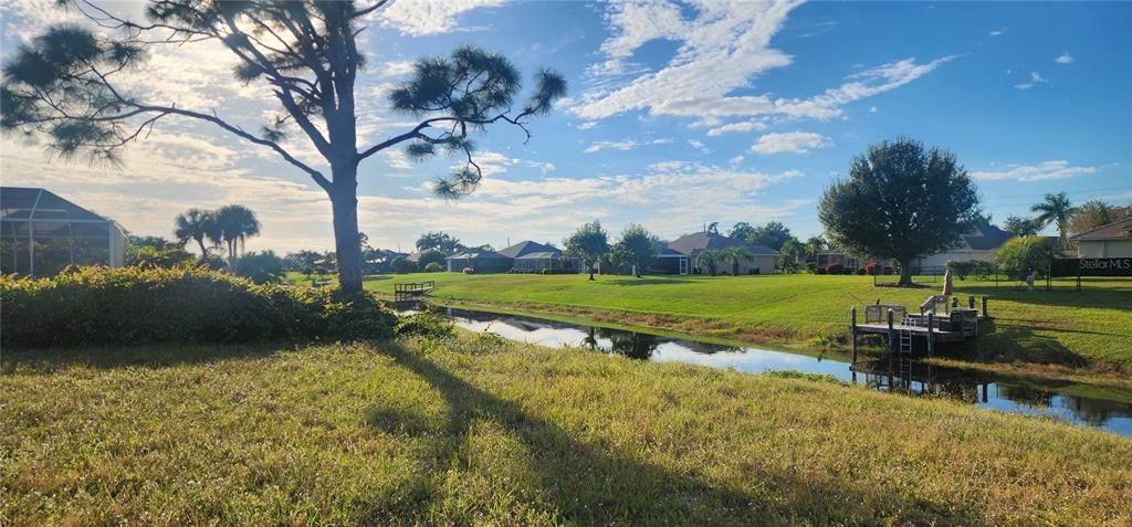 A grassy backyard overlooks a narrow canal with a wooden dock and distant suburban houses — 437 ROTONDA CIRCLE, ROTONDA WEST, FL