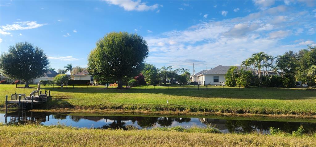 A grassy backyard with a small wooden dock overlooks a narrow canal and houses — 437 ROTONDA CIRCLE, ROTONDA WEST, FL