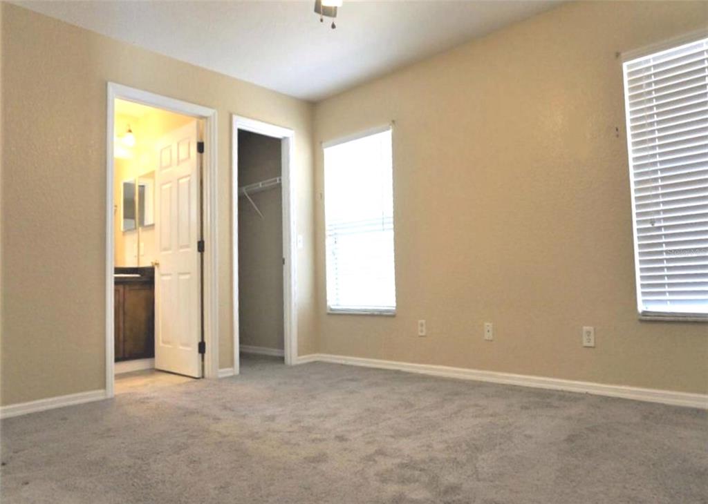 A bedroom with beige walls, gray carpeting, two windows with blinds, and two open doorways — 9435 N MANASHEE DRIVE, CITRUS SPRINGS, FL
