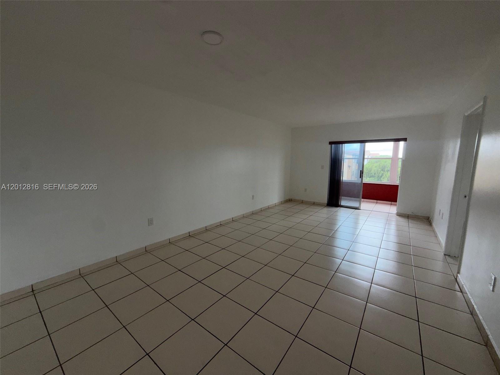 An empty room features white walls, beige tile flooring, and a sliding glass door — 120 Royal Palm Rd # 301, Hialeah Gardens FL 33016, HIALEAH GARDENS, FL