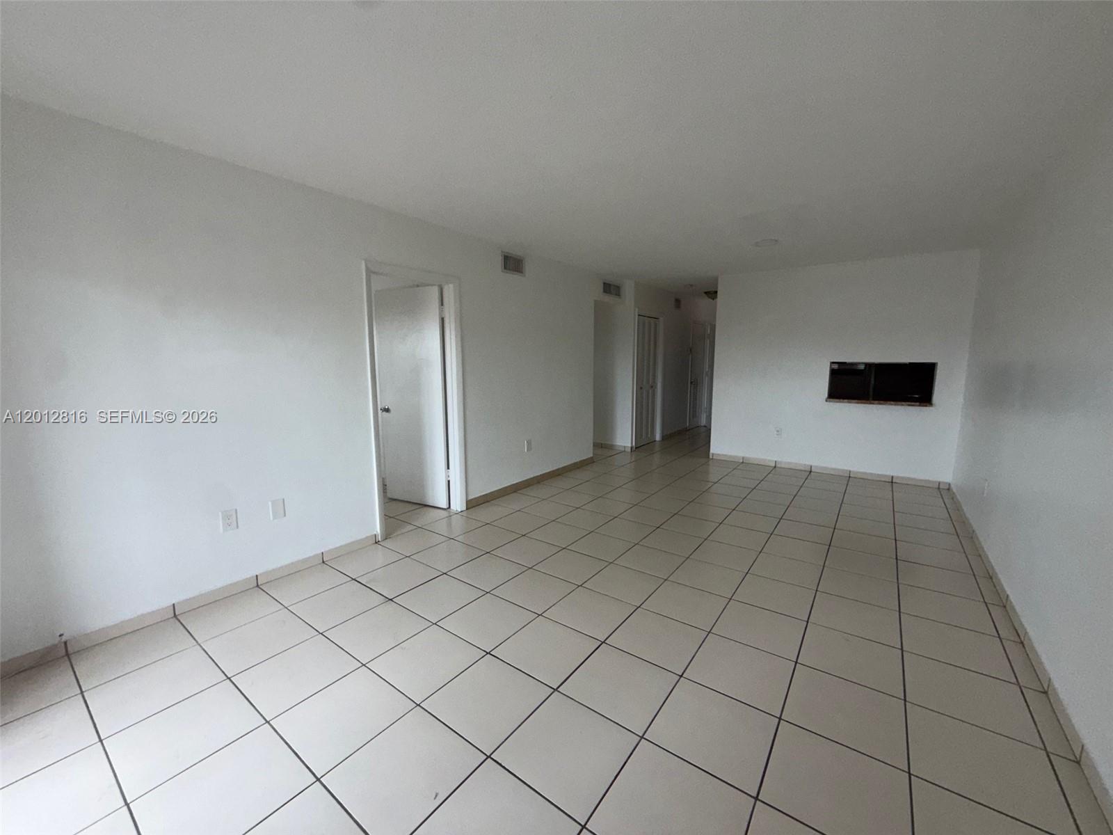 An empty room with white walls and light-colored square floor tiles features several doorways — 120 Royal Palm Rd # 301, Hialeah Gardens FL 33016, HIALEAH GARDENS, FL