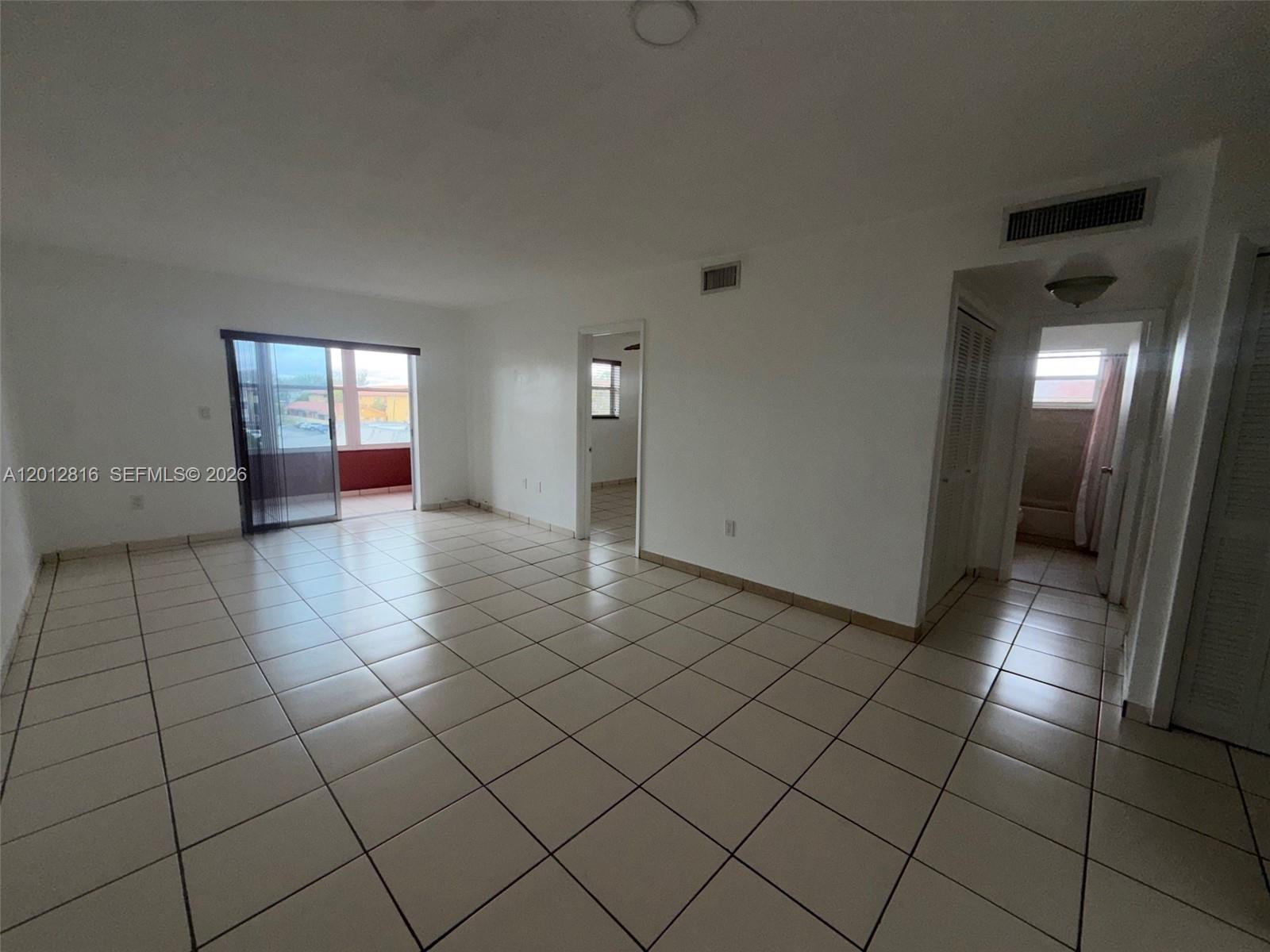 An empty room features white walls, light-colored floor tiles, and a sliding glass door — 120 Royal Palm Rd # 301, Hialeah Gardens FL 33016, HIALEAH GARDENS, FL