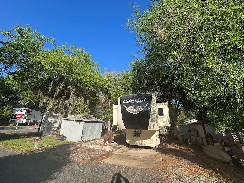 A Cedar Creek fifth-wheel trailer is parked on a concrete pad beneath large oak trees — 25238 NE 144TH STREET UNIT 144, FORT MC COY, FL