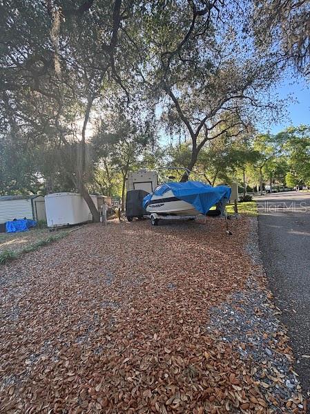 A boat covered by a blue tarp sits on a gravel lot under large trees — 25238 NE 144TH STREET UNIT 144, FORT MC COY, FL