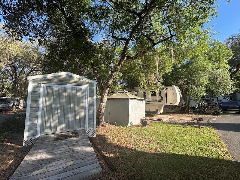 A storage shed with a wooden ramp sits near a parked RV under large trees — 25238 NE 144TH STREET UNIT 144, FORT MC COY, FL