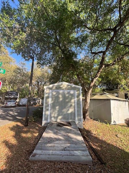 A light-colored storage shed sits at the end of a wooden walkway under large trees — 25238 NE 144TH STREET UNIT 144, FORT MC COY, FL