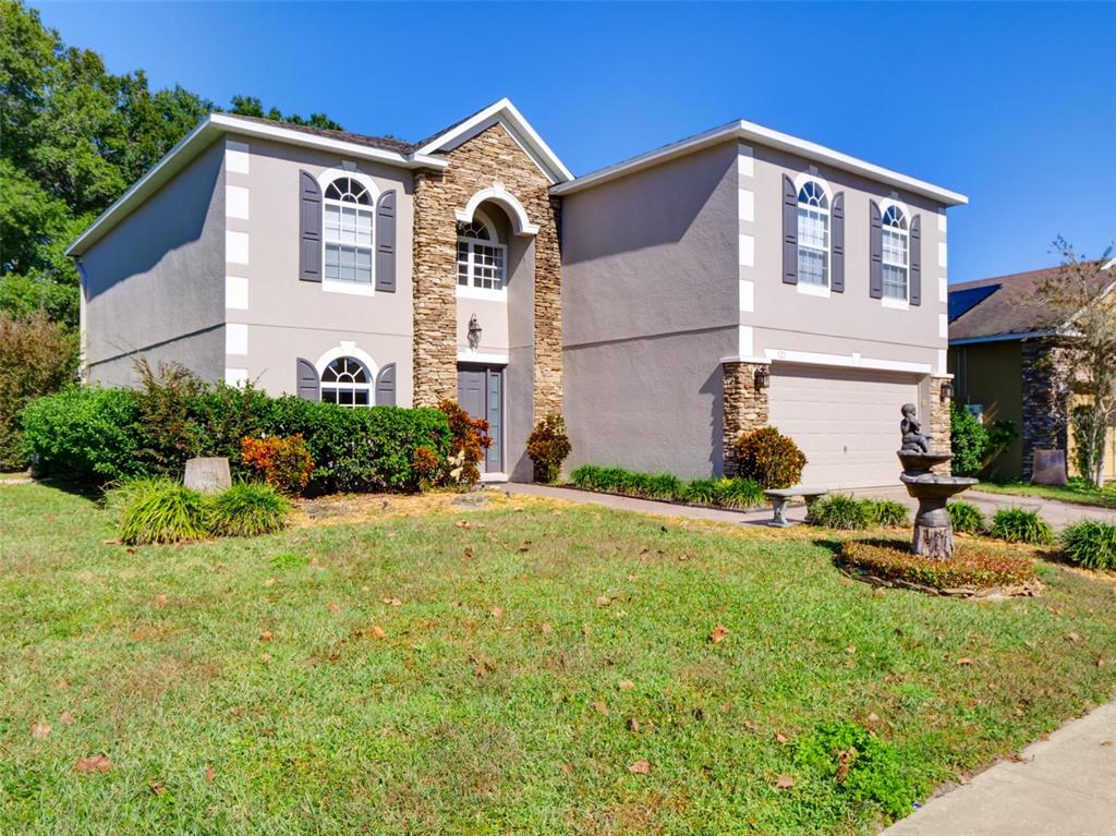 A two-story house with a stone facade, stucco exterior, and a front yard fountain — 121 W FIESTA KEY LOOP, DELAND, FL