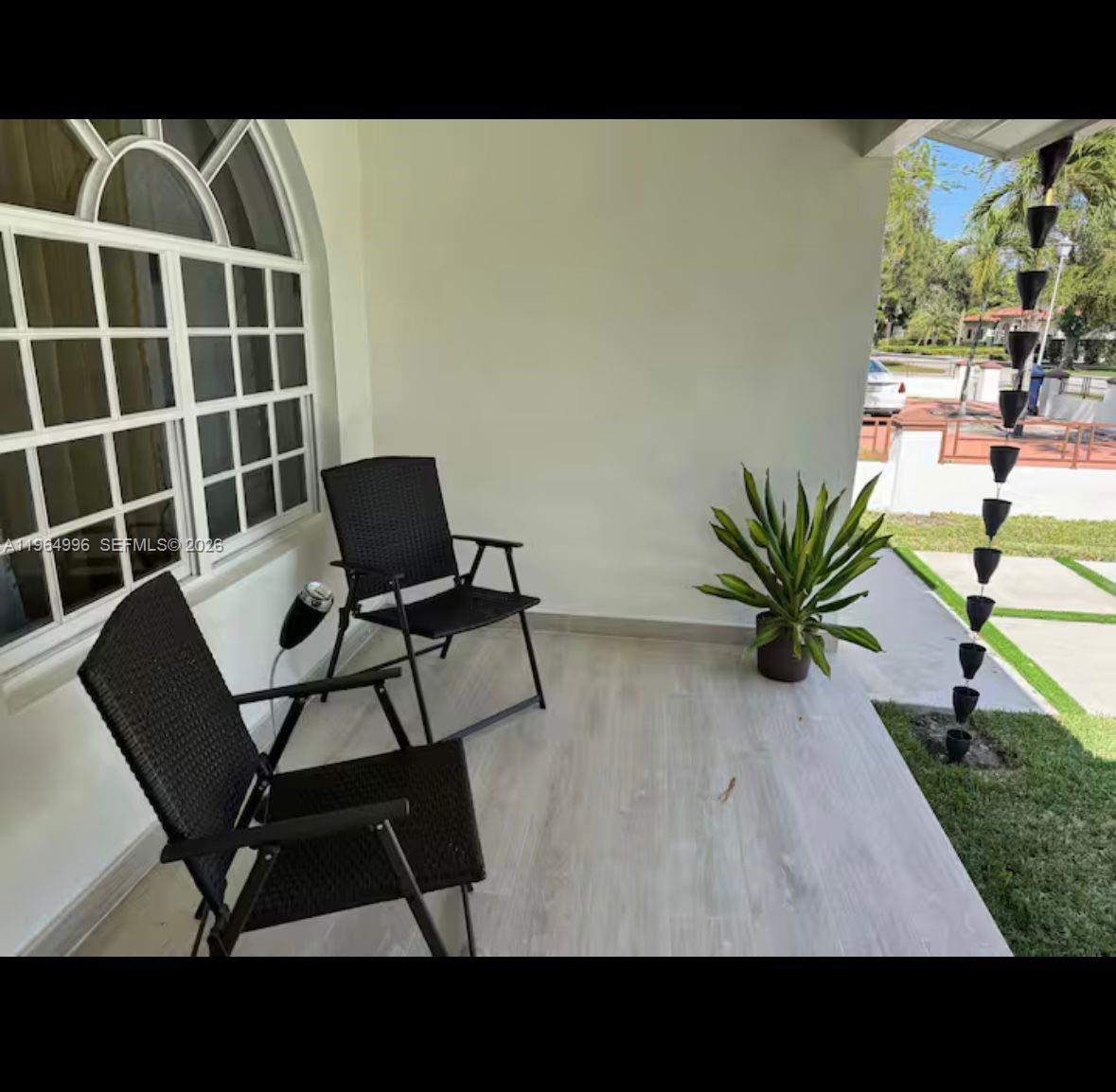 A covered patio features light wood-look flooring, two black chairs, and a potted plant — 508 De Leon Dr, Miami Springs FL 33166, MIAMI SPRINGS, FL