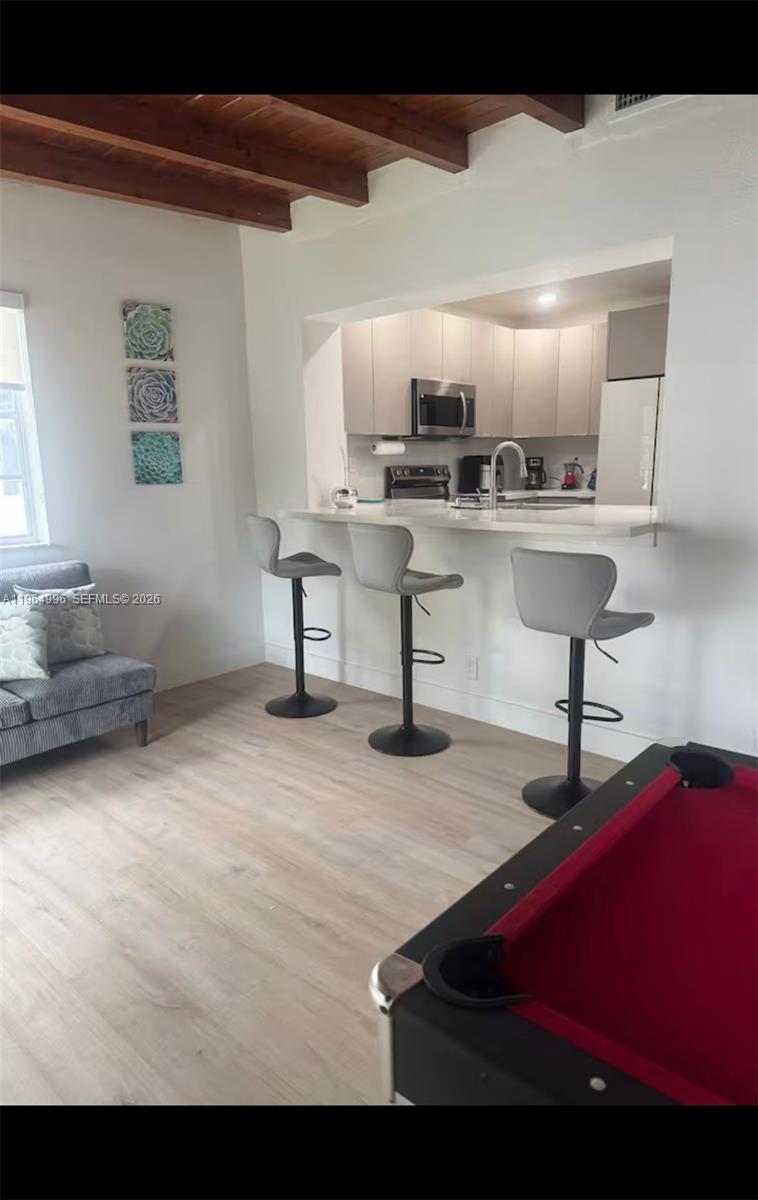 A kitchen with a breakfast bar and three stools overlooks a living area with a pool table — 508 De Leon Dr, Miami Springs FL 33166, MIAMI SPRINGS, FL