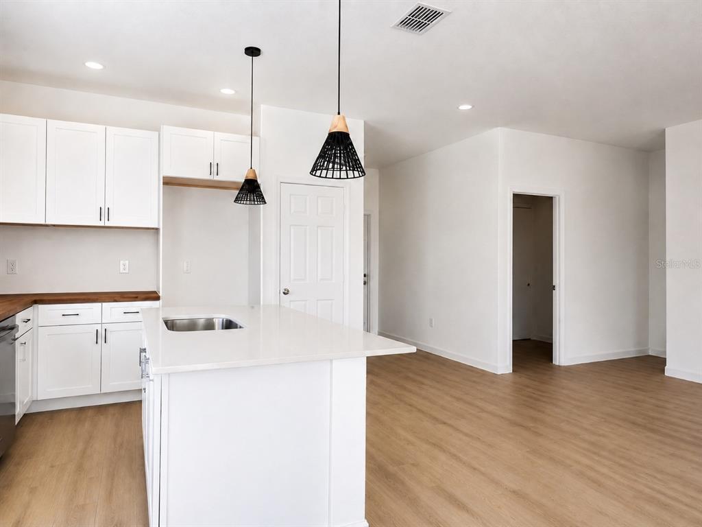 A modern kitchen features white cabinets, a central island with a sink, and pendant lighting — 980 TAHITI AVENUE SE, PALM BAY, FL