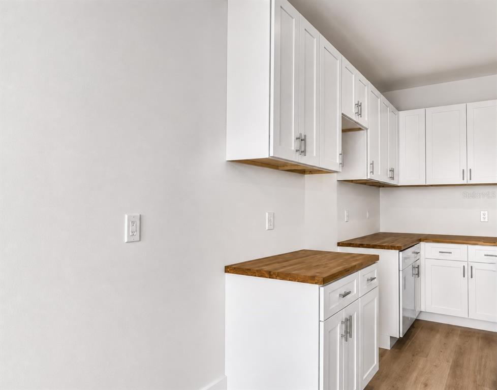 A kitchen features white shaker cabinets, wood countertops, and light wood-look flooring — 980 TAHITI AVENUE SE, PALM BAY, FL