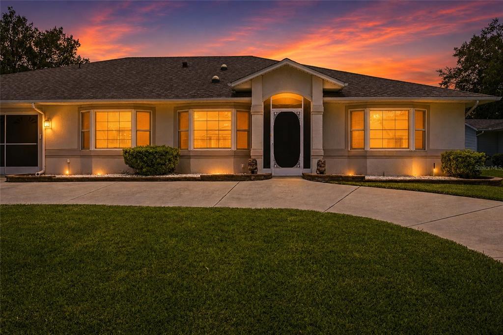 A single-story house exterior with a concrete driveway and a sunset sky — 27202 RACQUET CIRCLE, LEESBURG, FL