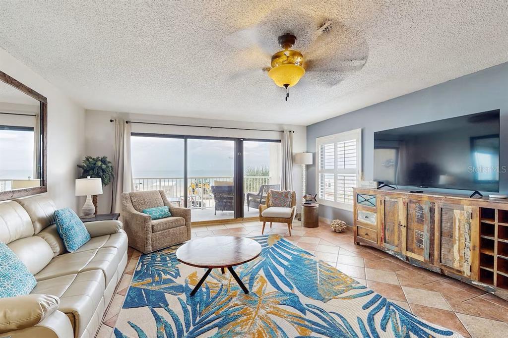 A living room features tile floors, a patterned area rug, a ceiling fan, and balcony access — 19236 GULF BOULEVARD UNIT 104, INDIAN SHORES, FL