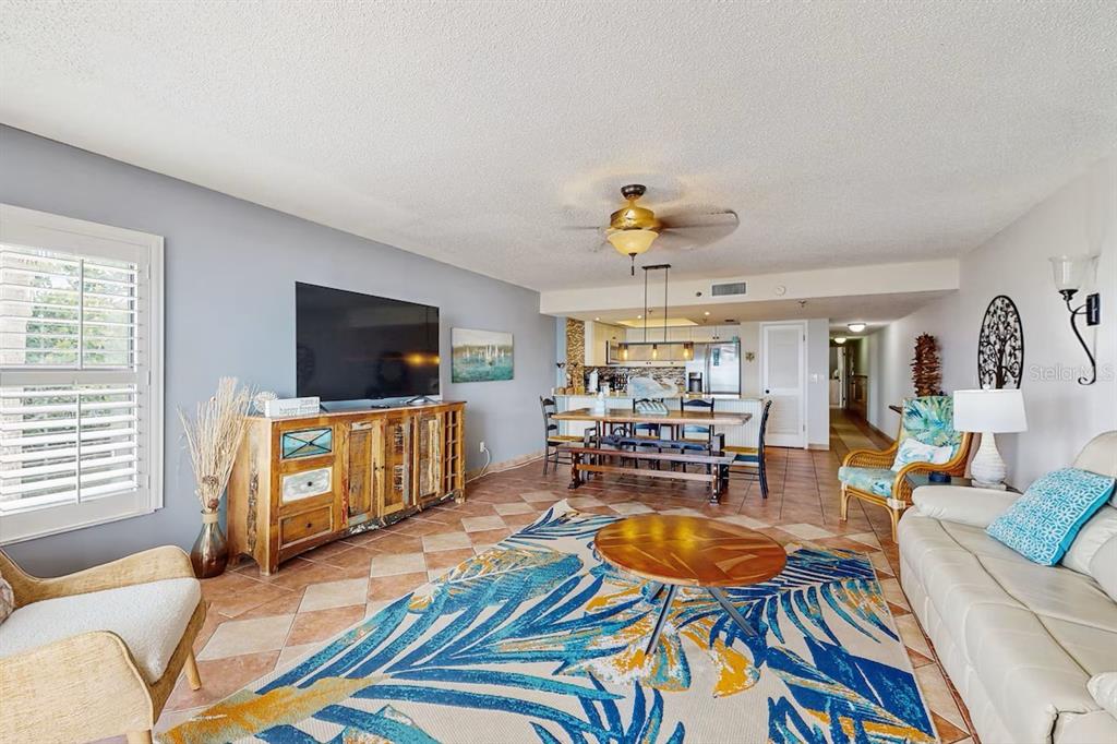 A living room with tile floors, a large area rug, and an open-concept dining area — 19236 GULF BOULEVARD UNIT 104, INDIAN SHORES, FL