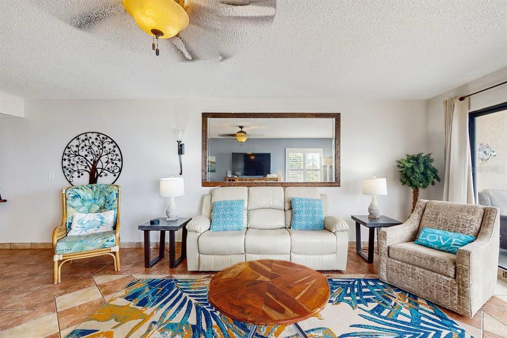 A living room features a white sofa, two armchairs, a coffee table, and a large mirror — 19236 GULF BOULEVARD UNIT 104, INDIAN SHORES, FL