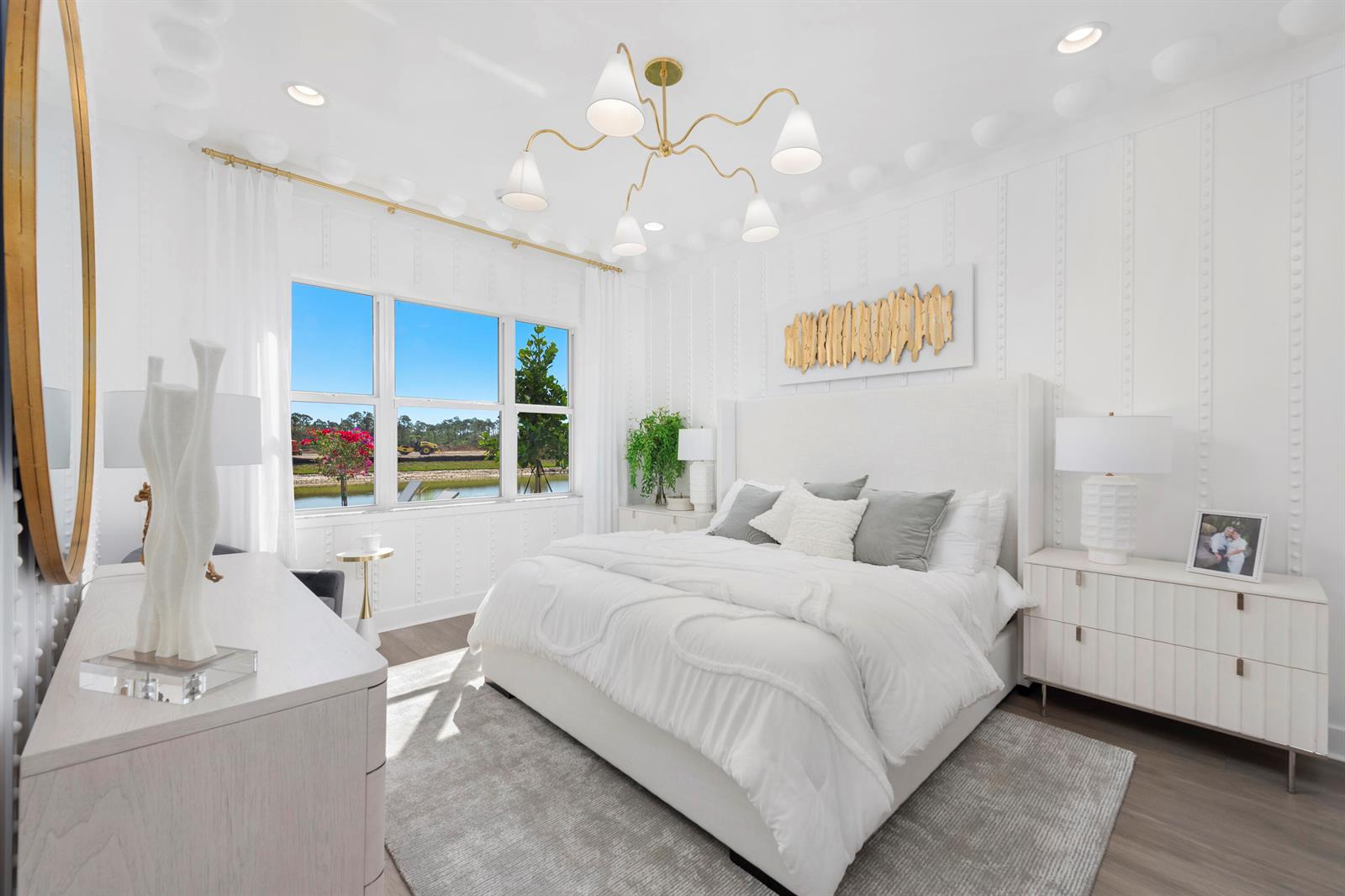 A bright bedroom features a white upholstered bed, gold chandelier, and a view of water — 481 40th Street, West Palm Beach FL 33407, WEST PALM BEACH, FL