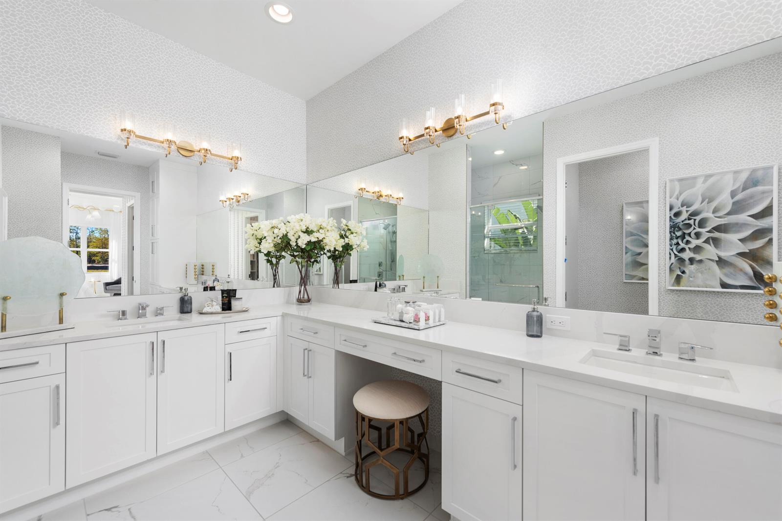 A bright bathroom features white cabinetry, dual sinks, a makeup vanity, and patterned wallpaper — 481 40th Street, West Palm Beach FL 33407, WEST PALM BEACH, FL