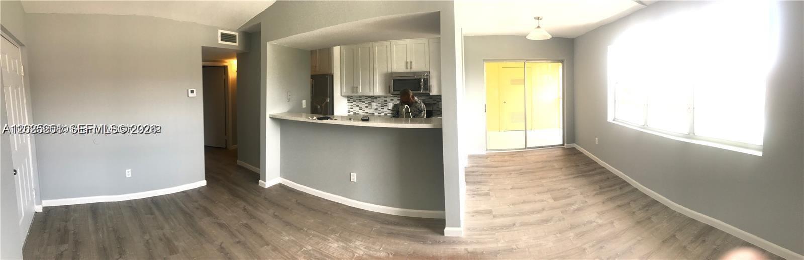This panoramic view shows an open-concept living area with wood-look flooring and a kitchen — 15285 SW 107th Ln # 206, Miami FL 33196, MIAMI, FL